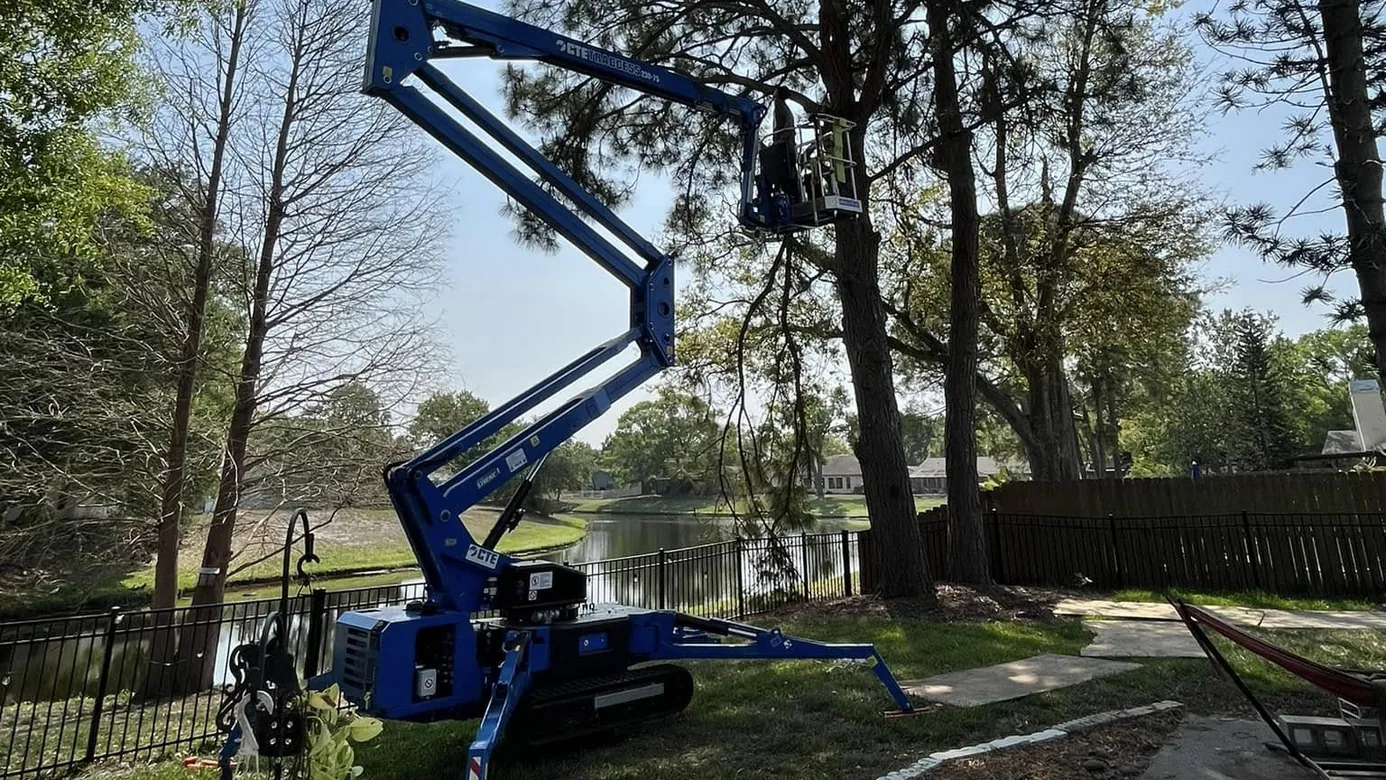 Tracked lift set up in a fenced back yard beside a pond, ready for tree work