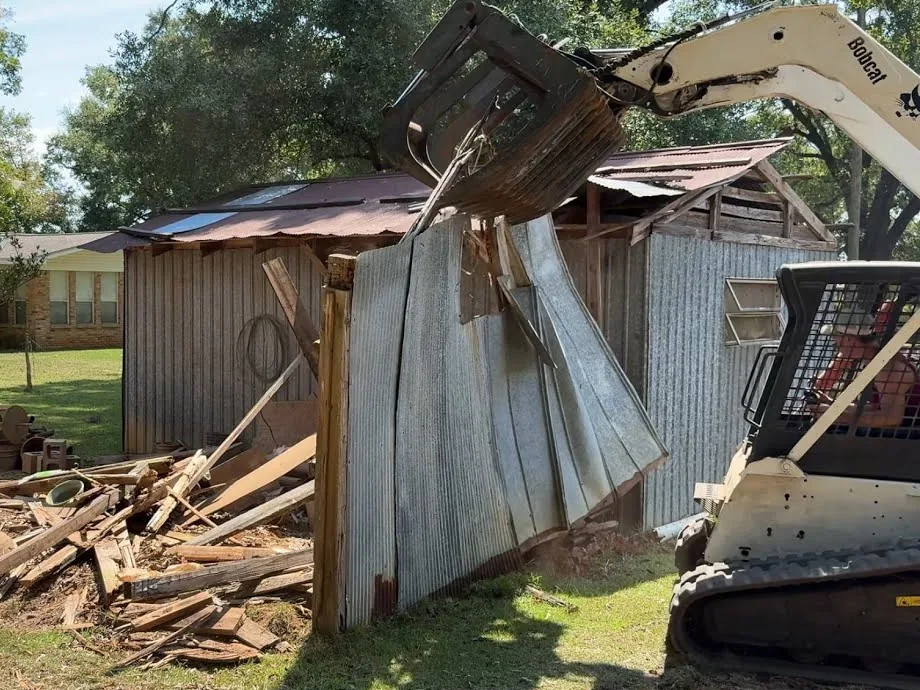 Shed demolition: a compact track loader with a grapple pulling down the metal wall of an old shed
