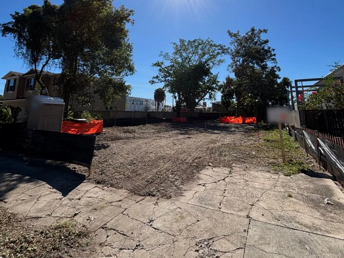 Site preparation: a cleared lot with orange safety fencing and trees left along the property line